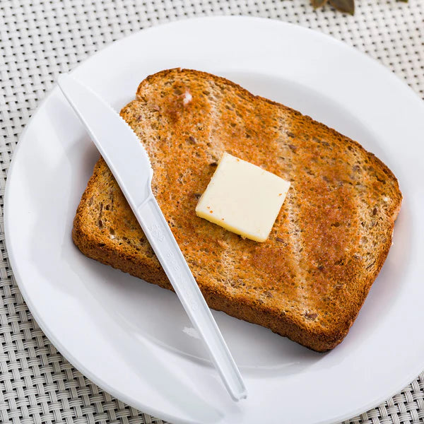 Toast with a pat of butter on a white plate with a disposable compostable party knife